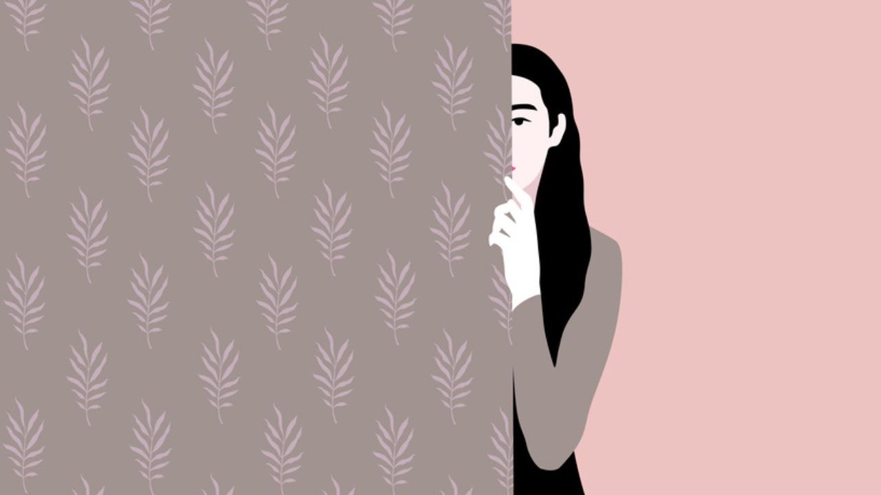 A woman with long hair hides behind a wall patterned in leaf wallpaper, only one eye visible as she looks straight out of the screen.