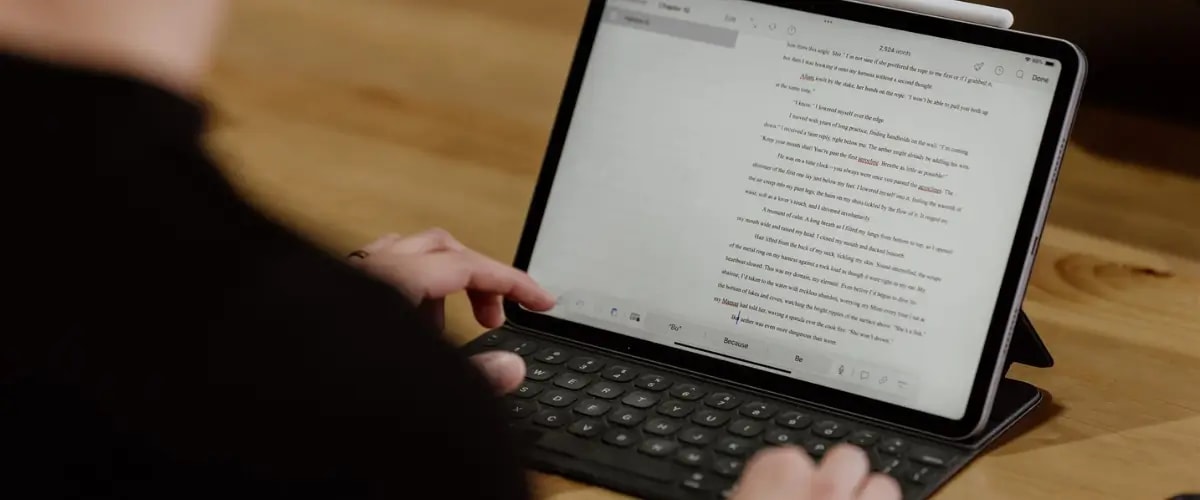 A writer types their manuscript onto an iPad using an attached keyboard.
