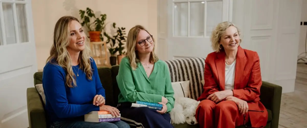Authors and writing coaches Colleen Oakley and Katie Khan sit on a sofa beside founder of The Novelry, Louise Dean, and her little white dog, Blue.