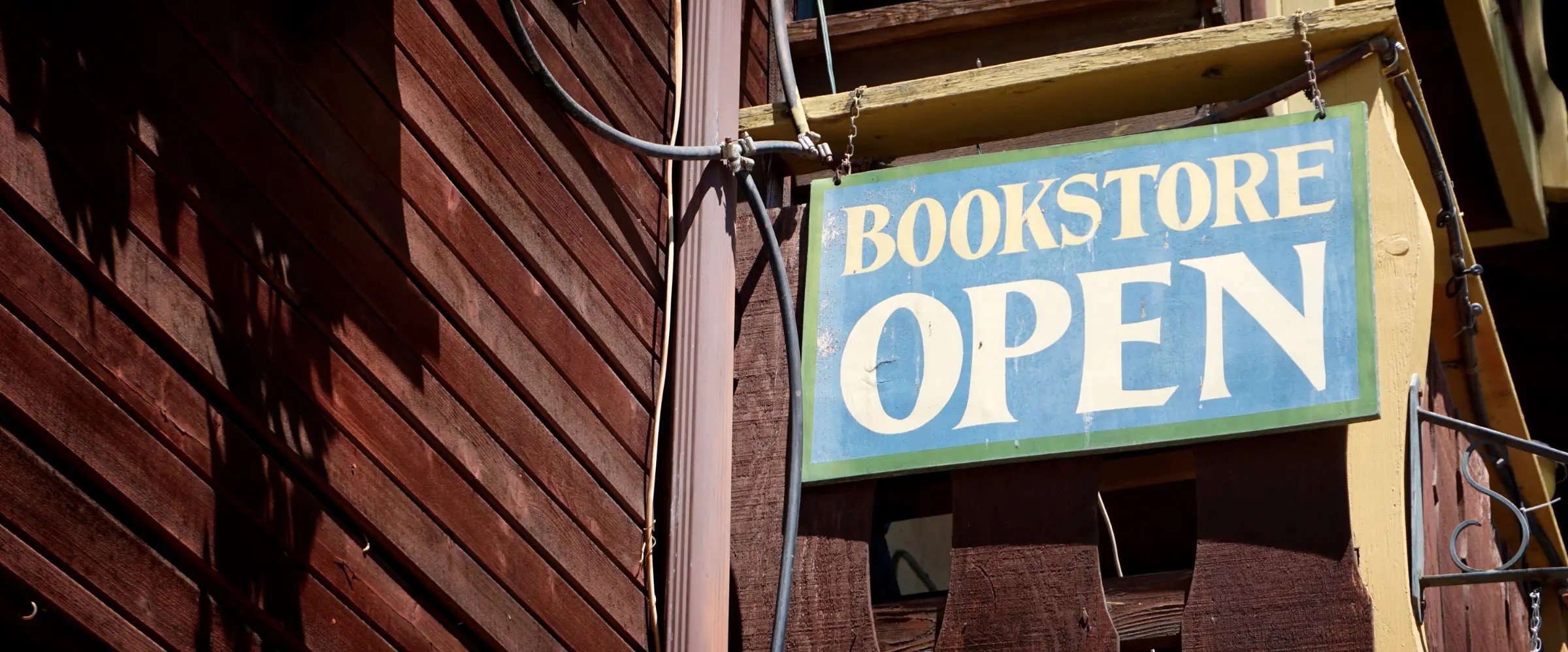 A sign outside a wood-slatted building reads: Bookstore Open.